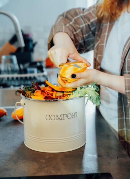 Compost kitchen waste; recycle at home. A compost bin with vegetable scraps on the kitchen table, with a blurred image of a woman cooking a meal. Environmentally responsible; ecology. Selective focus