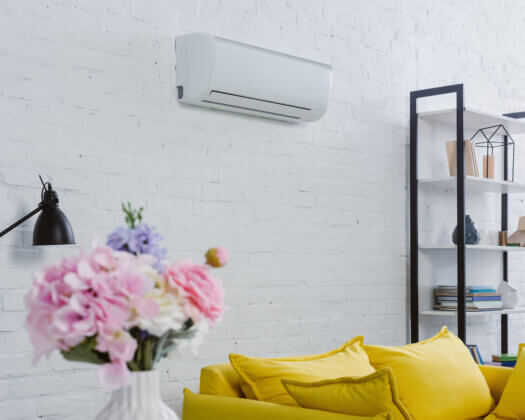 interior of modern living room with flowers in vase, yellow couch and air conditioner hanging on