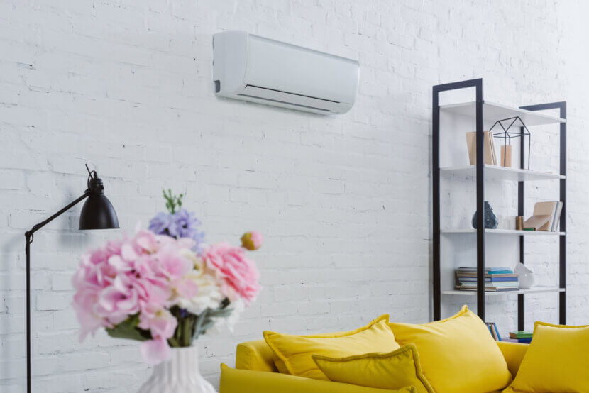 Interior of a modern living room with flowers in a vase, a yellow couch, and an air conditioner hanging on the wall