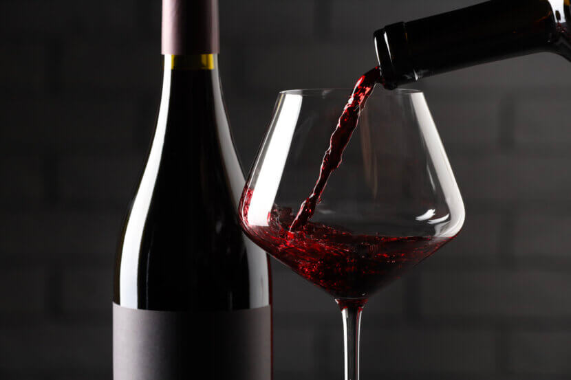 Pouring red wine into glass and bottles against brick wall background, closeup