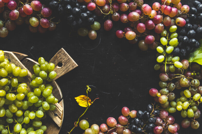An assortment of fresh grapes on a cutting board. Gray wooden background.