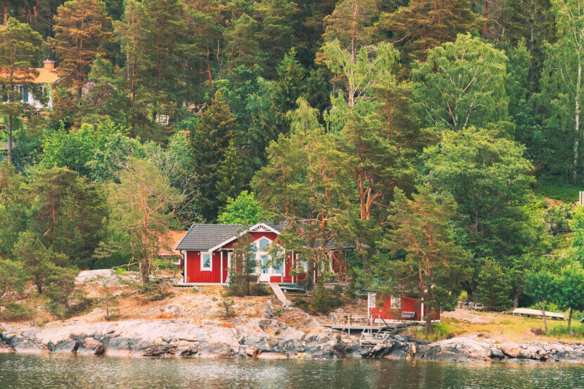 Sweden. Beautiful red Swedish wooden log cabins on the rocky island coast in summer. Lake or river landscape